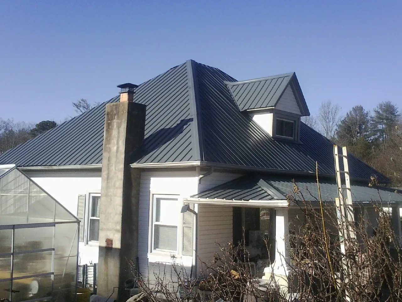 Dark blue standing seam metal roof on a white farmhouse with dormer — Slate & Tile Roof Repair by Roofing Brothers in East Aurora