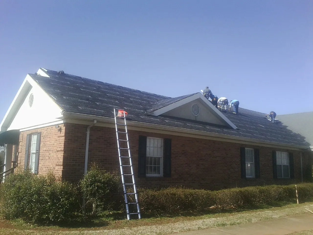 Crew tearing shingles off a brick ranch roof with a ladder set — Metal Roof Repair work by our crew in East Aurora