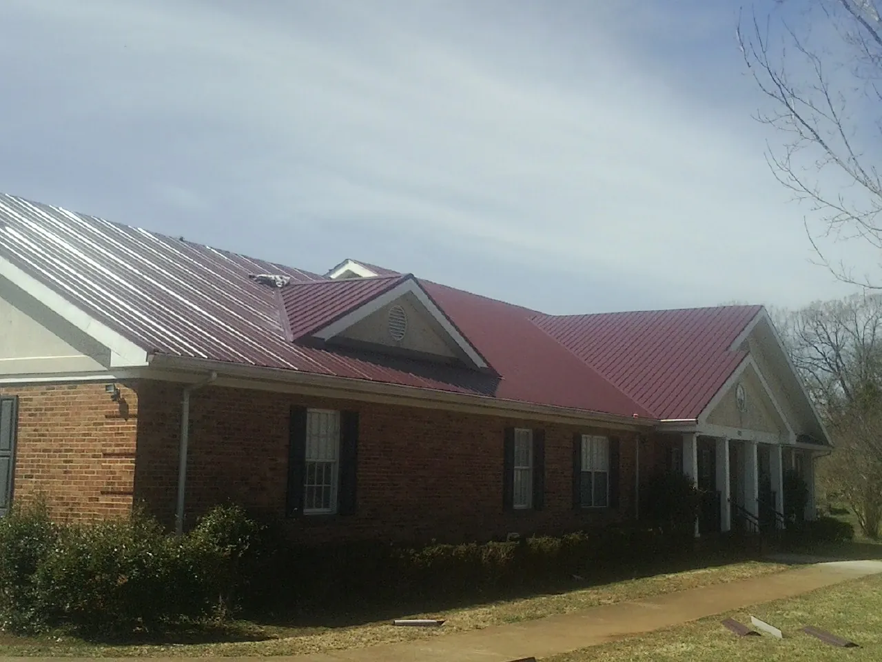 Red metal roof with gabled entries on a long brick building, from a Hail Damage Roof Repair job in East Aurora