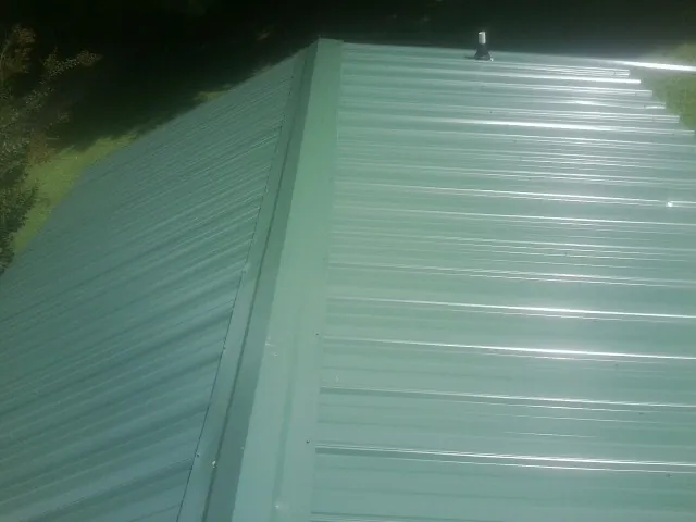 New green metal panels meeting at the ridge of a roof — Flat Roof Repair work by our crew in East Aurora