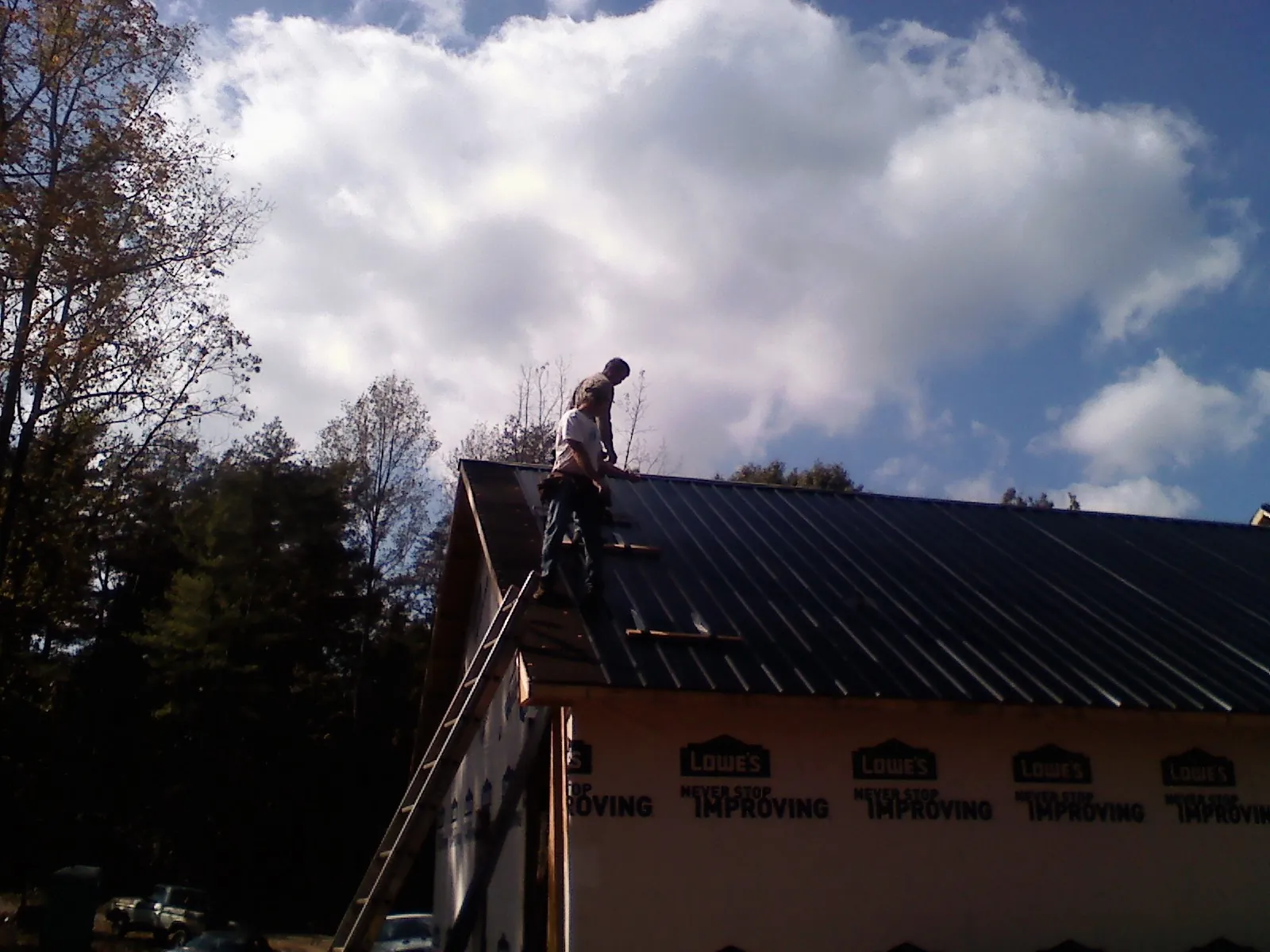 Roofer fastening dark metal panels high against a cloudy sky, from a Roof Inspection job in East Aurora