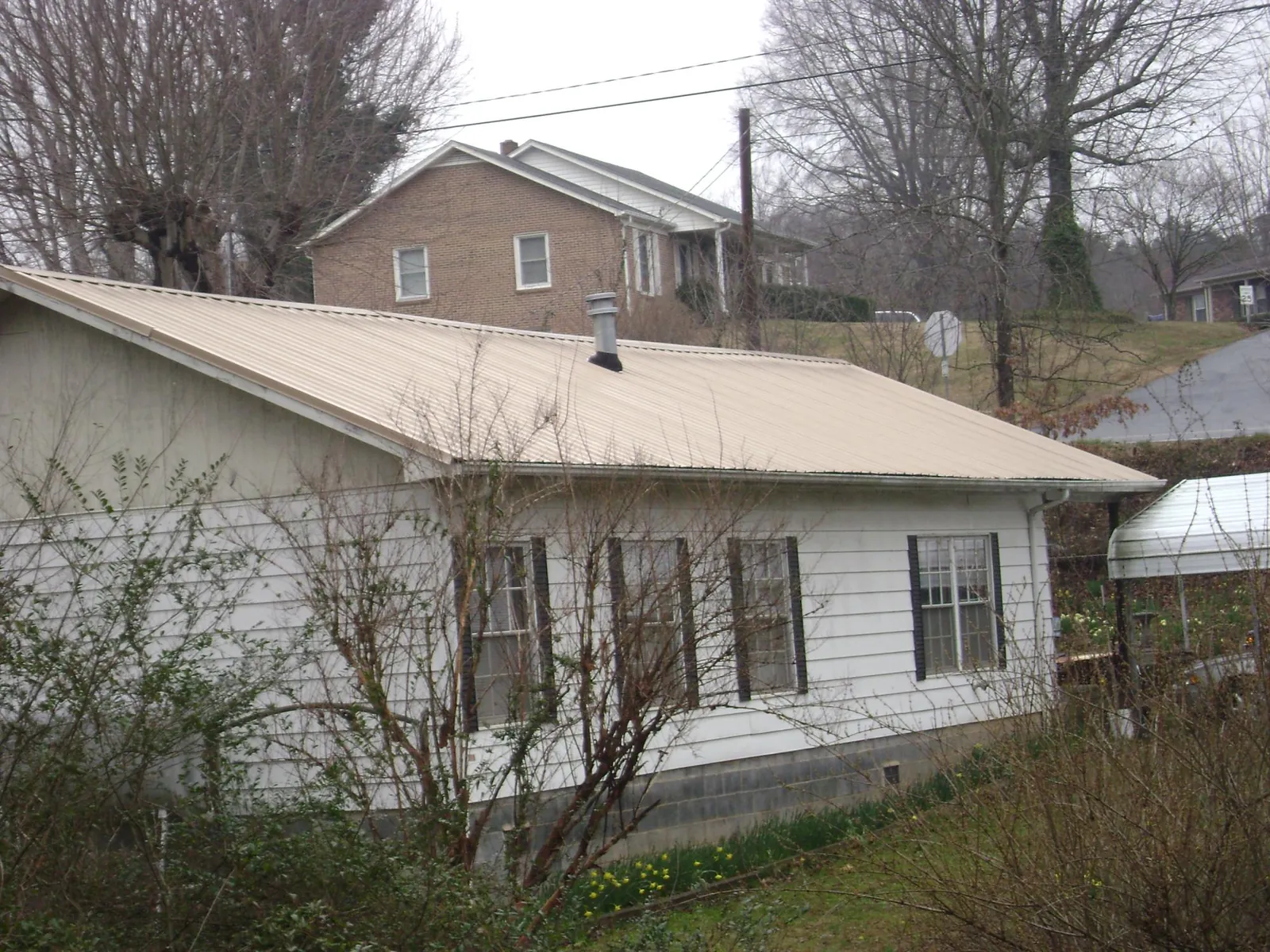 Tan metal roof on a white sided house set into a hillside — Commercial Roofing by Roofing Brothers in East Aurora